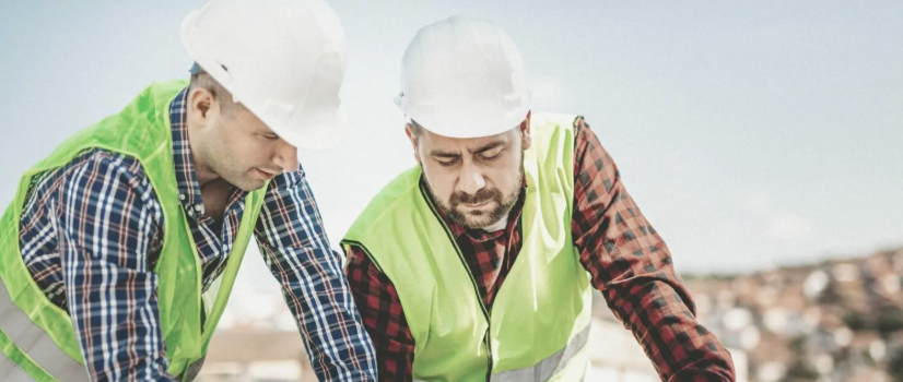 Copilot said:  Zwei Personen mit Schutzhelmen und Warnwesten betrachten gemeinsam technische Unterlagen auf einer Baustelle.
