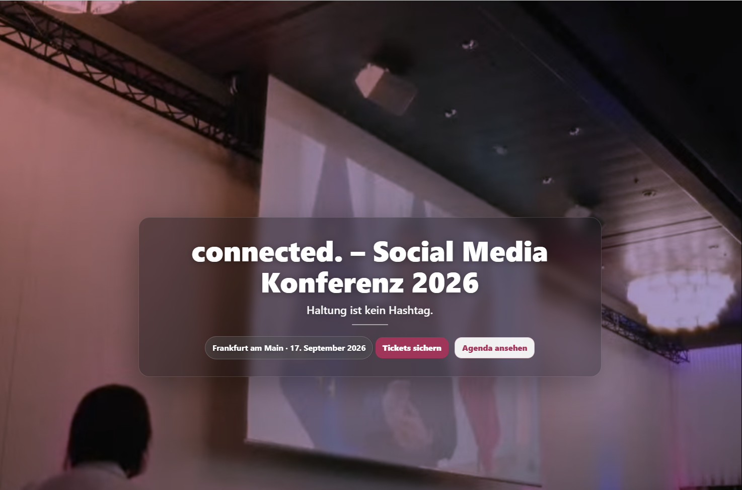 Werbegrafik für die „connected. – Social Media Konferenz 2026“ vor einer unscharfen Veranstaltungsbühne mit Projektionsfläche, Datum (17. September 2026) in Frankfurt am Main sowie Schaltflächen für Tickets und Agenda.