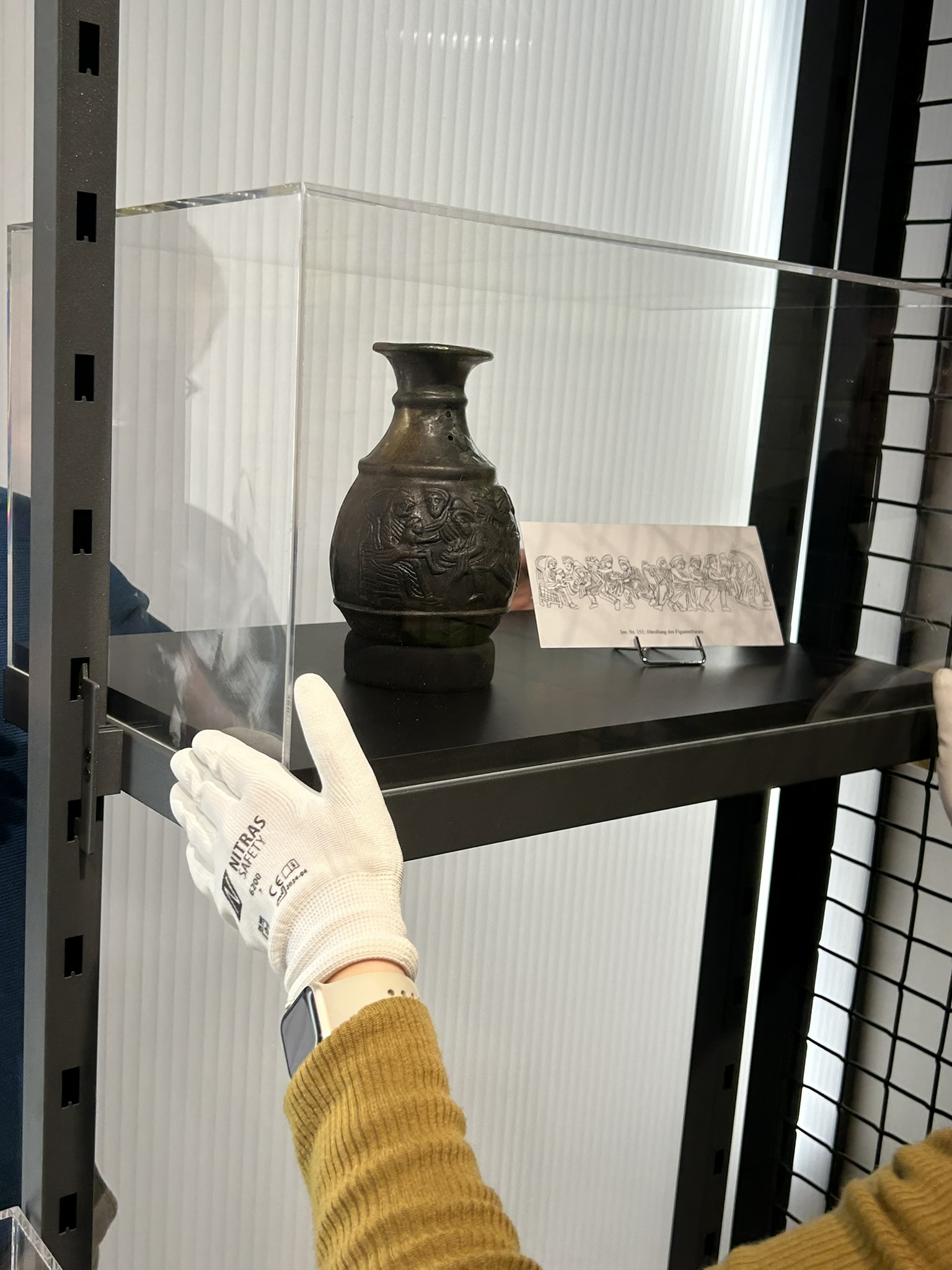 Befestigung einer Vitrine mit Messingkanne